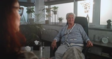 Yaşlı kadın terapiste rahatsızlığın semptomlarını anlatıyor, travmatik deneyimleri paylaşıyor. Kadın psikoterapist seans sırasında dinler ve not defterine yazar. Psikoloji ve akıl sağlığı kavramı.