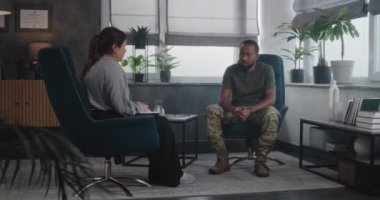 Travma sonrası stres bozukluğu olan depresif Afrikalı Amerikalı erkek asker terapist ile konuşuyor terapi seansı sırasında travmatik deneyimleri paylaşıyor. Kadın askeri psikolog elinde defterle sandalyede oturur ve erkekleri dinler..