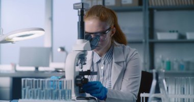 Parlak tıp bilimi laboratuvarı: Kadın biyokimyacı test tüpünden sıvı alır, mikroskop altında inceler, örnek analizi yapar. Bilim adamı ve mikrobiyolog yüksek teknolojili ekipmanlar kullanarak ilaç geliştiriyor..