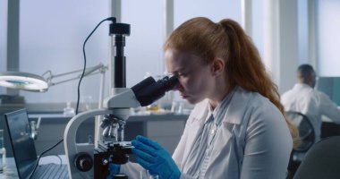 Mikroskop altında incelemek ve incelemek için koruyucu gözlük takan kadın bilim adamı veya kimyager dizüstü bilgisayar kullanır. Arka planda analiz yapıyor. Modern Tıp Laboratuvarı.