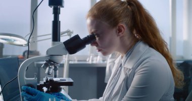 Modern tıp laboratuvarında yüksek teknolojili ekipmanlarla, güzel kadın mikrobiyolog veya kimyager mikroskopla çalışır ve dizüstü bilgisayar kullanır. Tıbbi testler ve deneyler. Eczacılık firması. Kapat..