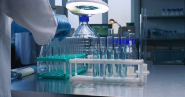 İleri düzey tıbbi araştırma laboratuvarı: eldiven giyen kimyager ya da bilim adamlarına yakın çekim yapmak ve analiz için mavi sıvıyı test tüplerine koymak. Modern farmakoloji laboratuvarı. Biyoteknoloji geliştirme.