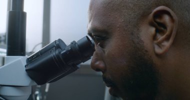 Afrika kökenli Amerikalı erkek mikrobiyolog mikroskop altında numuneleri inceliyor. Profesyonel bilim adamı, kimyager yüksek teknolojili ekipman kullanıyor. Bilimsel araştırma.
