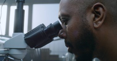 Afrika kökenli Amerikalı erkek mikrobiyolog mikroskop altında numuneleri inceliyor. Profesyonel bilim adamı, kimyager yüksek teknolojili ekipman kullanıyor. Bilimsel araştırma.