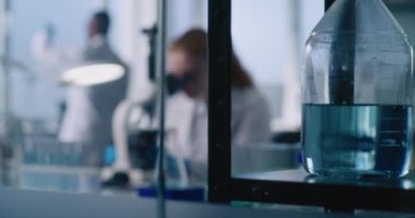 Genç dişi mikrobiyolog mikroskop altında yeni örnekler ekliyor, sonuçları inceliyor ve karşılaştırıyor. Arka planda, erkek bilim adamı örnekler üzerinde çalışıyor. Gelişmiş Tıp Bilimleri Laboratuvarı.