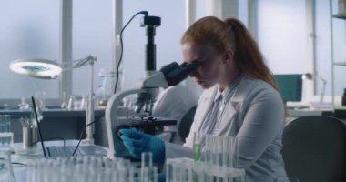Parlak tıp bilimi laboratuvarı: Dişi mikrobiyolog mikroskop altında inceler, test örneklerini analiz eder, güvenlik gözlüğü takar. Bilim adamı, biyokimyacı yüksek teknoloji ekipmanları ve dizüstü bilgisayarla çalışıyor..