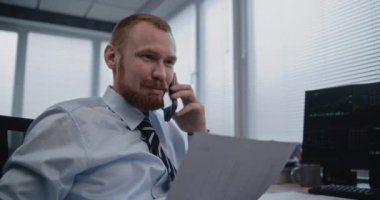 Borsa işlemlerini sonuçlandırmak için ortakla akıllı telefondan iletişim kuran tüccarın portresi. Finans şirketinin yakışıklı erkek çalışanı başarılı iş görüşmeleri yürütüyor.