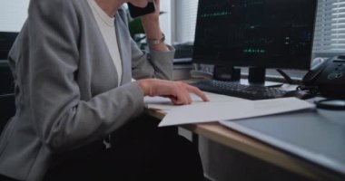 Kağıt dökümanları ve finansal ölçümlerle çalışan kadın finansörlerin kapatılması, cep telefonuyla iş müşterileriyle iletişim kurulması. Bilgisayar ekranında borsa ve satışlar görülüyor. Finans ve bankacılık.
