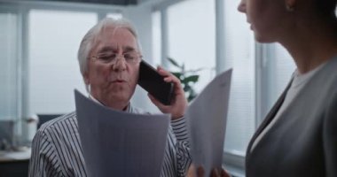 Kıdemli şirket başkanı iş ortağıyla cep telefonundan iletişim kuruyor. Kadın finans çalışanı elinde belgelerle, patronunu dinliyor. Banka veya uluslararası şirketin modern ofisi.
