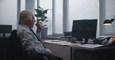 Modern ofiste: Yorgun kıdemli finans çalışanı kahve içiyor, gazete ve belgeleri analiz ediyor, erkek meslektaşıyla konuşuyor. PC ekranında sermaye piyasası ve hisse senetleri görülüyor. Uluslararası borsa şirketi.