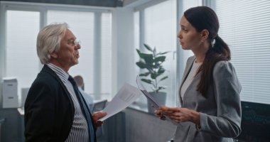 Elinde kağıt belgeler tutan iki profesyonel finans uzmanı proje fikirlerini tartışıyor, beyin fırtınası yapıyor ve iş stratejisi geliştiriyor. Üst düzey patron ve bayan çalışan modern ofiste tartışıyorlar..