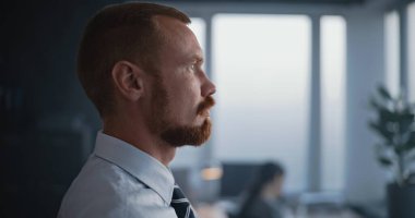 Modern ofiste: Pencerelerin karşısında duran yorgun ve düşünceli finans tüccarı veya profesyonel bankacı, proje fikirleri veya iş stratejisi hakkında düşünüyor. Yakın çekim. Portre.