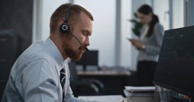 Profesyonel borsa simsarı modern ofiste çalışıyor. Kulaklık konusunda bilgisayar uzmanı, müşterilerle konuşuyor, gözlemciler pazarları paylaşıyor, notlar alıyor. Arka plandaki bayan meslektaşım..