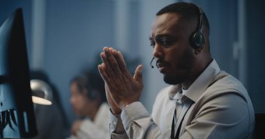 Ruh sağlığı hattının modern çağrı merkezi: Afrika kökenli Amerikalı yardım hattının portresi bilgisayarın başında oturan, dinleyen, çevrimiçi psikolojik yardım sağlayan kulaklık uzmanı.