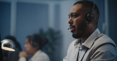 Ruh sağlığı hattının modern çağrı merkezi: Afrika kökenli Amerikalı yardım hattının portresi bilgisayarın başında oturan, dinleyen, çevrimiçi psikolojik yardım sağlayan kulaklık uzmanı.