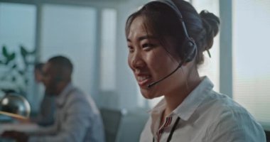 Dost canlısı Asyalı kadın yardım hattı uzmanı kulaklıkla konuşuyor, müşteri hizmetleri sağlıyor. Modern çağrı merkezinde çalışan çok ırklı teknik destek operatörleri ekibi. Çevrimiçi müşteri yardımı.
