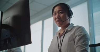 Çağrı merkezi: Asyalı kadın yardım masası uzmanının portresi çağrı üzerine konuşma, bilgisayar üzerinde çalışma, çevrimiçi müşteri hizmetleri sağlama. Teknik destek operatörü çalışıyor.