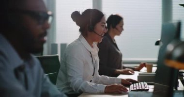 Merkez ofisi: Kulaklıklarda çalışan çok ırklı operatörlerden oluşan bir ekip. Asyalı müşteri destek uzmanı telefonla konuşuyor, bilgisayarda çalışıyor, müşteriye çevrimiçi yardım sağlıyor.