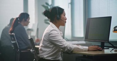 Modern çağrı merkezinde çalışan çok ırklı teknik destek operatörleri ekibi. Asyalı kadın yardım masası uzmanı çağrı yoluyla danışmanlık yapıyor, bilgisayar kullanıyor, müşteri hizmetleri sağlıyor.