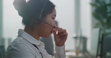 Modern çağrı merkezi: Asyalı teknik destek uzmanının kulaklık kullanarak müşteriyle konuşması. Kadın yardım hattı operatörü müşteriye çevrimiçi yardım sağlayan bir bilgisayar kullanıyor. Portre.