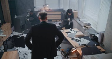 Ofis soygunu, olay yerini inceleyen dedektifin yüksek açısı, ipucu arayan kadın kriminalist, parmak izi arayan Afro-Amerikan polisi. Suç araştırma ekibi çalışıyor.