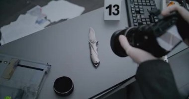 Soygun ya da cinayet davası: Adli tıp uzmanının profesyonel kamerayla cinayet silahının fotoğrafını çekerken yakın plan çekimi. Delillerin yanında numaralandırılmış işaret var. Kriminolog suç mahallinde çalışıyor.