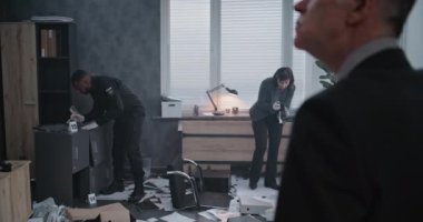 Ofis soygunu davası: suç araştırma ekibi çalışıyor. Erkek dedektif olay yerini inceliyor, kadın adli tıp uzmanı ipuçlarının fotoğrafını çekiyor, Afrikalı Amerikalı polis memuru parmak izlerini arıyor..