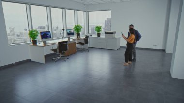 Multiethnic team of two designers using app on tablet computer to design interior in office room with 3D furniture and digital equipment in virtual space. Futuristic VFX animation. Augmented reality.