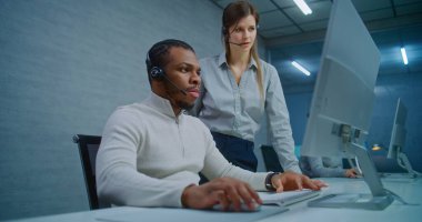 Modern çağrı merkezi ofisi: Kulaklıktaki iki çoklu etnik yardım hattı operatörü konuşuyor ve bilgisayarda iş izleme verilerini tartışıyor. Çevrimiçi müşteri desteği üzerinde çalışan teknik destek uzmanları..