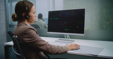 Beyaz kadın uluslararası şirketin modern ofisinde çalışıyor: Kadın borsa simsarları kulaklıkla konuşuyor, sermaye piyasasını ve bilgisayar kullanarak hisseleri izliyor, grafikleri analiz ediyor, diyagramları inceliyor. E-ticaret.