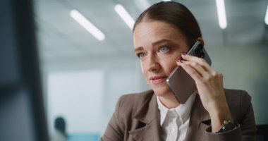 Beyaz kadın parlak gelişmiş bir ofiste çalışıyor: Stresli kadın pazarlama uzmanı veya müşteri yöneticisi iş ortağı veya müşteriyle telefonla agresif bir şekilde konuşuyor, bilgisayar ekranına bakıyor. E-iş.