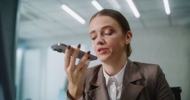 Beyaz kadın modern ofiste çalışıyor: Kadın pazarlama uzmanı veya müşteri yöneticisi iş yerinde oturuyor, iş ortağı veya müşterisiyle iletişim kuruyor, akıllı telefondan sesli mesaj kaydediyor. E-iş