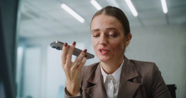Beyaz kadın modern ofiste çalışıyor: Kadın pazarlama uzmanı veya müşteri yöneticisi iş yerinde oturuyor, iş ortağı veya müşterisiyle iletişim kuruyor, akıllı telefondan sesli mesaj kaydediyor. E-iş