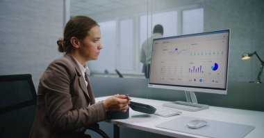 Beyaz kadın finans uzmanı ya da E-ticaret müdürü öğle arasında iş yerinde yemek yiyor. PC ekranında ticari veriler ve diyagramlar var. E-ticaret şirketinin modern ofisi.