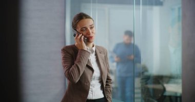 Kafkasyalı başarılı iş kadını cep telefonuyla iş anlaşması hakkında konuşuyor, yeni proje veya şirket stratejisini partneriyle tartışıyor. Kadın pazarlama uzmanı donanımlı E-ticaret ofisinde çalışıyor..