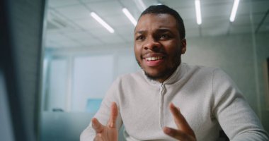 Afrika kökenli Amerikalı bir adam ileri düzey bir ofiste çalışıyor: Mutlu pazarlama uzmanı veya müşteri yöneticisi bilgisayar kullanan, sevinen ve başarılı anlaşmayı kutlayan iş ortağı veya müşteriyle sohbet ediyor. E-iş.