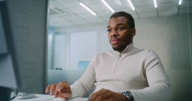 Afrika kökenli Amerikalı bir adam ileri düzey bir ofiste çalışıyor: Mutlu pazarlama uzmanı veya müşteri yöneticisi bilgisayar kullanan, sevinen ve başarılı anlaşmayı kutlayan iş ortağı veya müşteriyle sohbet ediyor. E-iş.