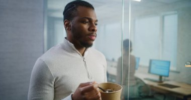 Afro-Amerikalı işadamı ya da ofis çalışanı öğle arasında ara vererek teslimattan yemek yiyor. E-ticaret şirketinin modern ofisinde bilgisayar ile donatılmış profesyonel finans uzmanı.
