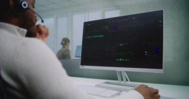 Afrikalı Amerikalı adam uluslararası şirketin modern ofisinde çalışıyor: borsa simsarları kulaklıkla konuşuyor, sermaye piyasasını izliyor ve bilgisayar kullanarak hisseleri takip ediyor, grafikleri ve şemaları analiz ediyor. E-ticaret