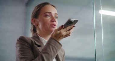 Modern ofis: Akıllı telefon kullanarak iş ortağına uygulamayla sesli mesaj kaydeden başarılı bir iş kadınını kapatın. Profesyonel kadın pazarlama uzmanı büyük bir E-ticaret şirketinde çalışıyor..