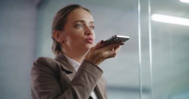 Profesyonel kadın e-ticaret müdürünün portresi cep telefonundan iş ortağına kurye uygulaması ile sesli mesaj kaydediyor. Başarılı iş kadını, E-ticaret şirketinin modern ofisinde çalışıyor..
