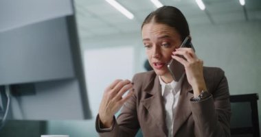 Öfkeli Kafkasyalı iş kadını iş ortağıyla konuşur ya da müşterisine telefonla danışır, iş yerinde oturur, kameraya bakar. Kadın pazarlama uzmanı modern ofiste çalışıyor. E-ticaret.