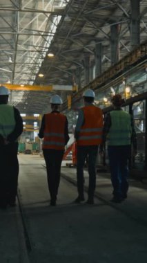 Üniformalı ve miğferli dört ağır endüstri teknisyeni üretim sürecini tartışıyor, fabrikada yürüyor. Erkek ve kadın müfettişler fabrika çalışanlarıyla konuşur. dikey