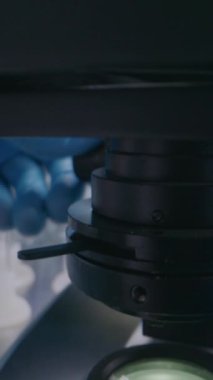 Tıbbi bilim laboratuvarı: Analiz için mikroskop kuran mikrobiyolog veya bilim adamına yakın çekim. Sıvı kimyasal madde numunesiyle birlikte cam kaydırma. Uyuşturucu geliştirme. Dikey çekim
