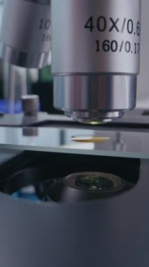 Uzman mikrobiyolog ya da eldivenli bilim adamının dikey çekimi. Analiz için mikroskop kuruyor, aşı geliştiriyor. Test örneğiyle birlikte cam kaydırma. Yüksek teknoloji laboratuvar ekipmanları.