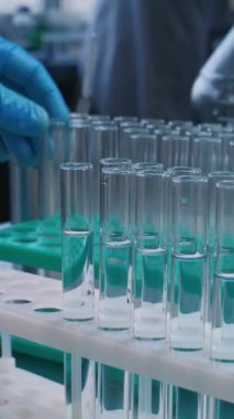 Tıbbi araştırma laboratuvarı: Bilimadamlarının cam mataradan mavi sıvıyı alıp analiz için test tüplerine döktüklerine yakın çekim. Gelişmiş farmakoloji laboratuvarı. Dikey çekim