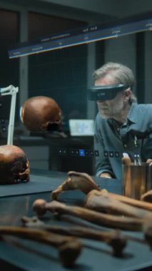 VR kulaklıklı dikey çekim arkeoloğu, fosil kafatası kullanarak eski insan anatomisini araştırıyor. Tarama yazılımı arayüzü ile sanal görüntünün 3 boyutlu canlandırması.