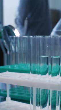 Tıbbi araştırma laboratuvarı: Bilimadamlarının cam mataradan mavi sıvıyı alıp analiz için test tüplerine döktüklerine yakın çekim. Gelişmiş farmakoloji laboratuvarı. Dikey çekim