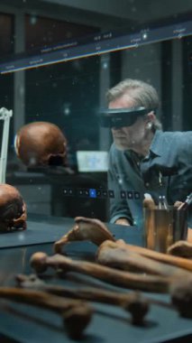 Dikey çekim, VR kulaklığında olgun bir arkeolog fosil kafatası kullanarak eski insan anatomisini araştırıyor. Yazılım kullanıcı arayüzü ile üç boyutlu sanal görüntü grafikleri. VFX