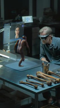 VR kulaklıklı dikey çekim arkeoloğu yapay zeka simülatöründe antik insan evrimini araştırıyor, artırılmış gerçekliği kullanarak araştırma yapıyor. Yapay zeka asistanıyla birlikte üç boyutlu sanal görüntü oluşturma. VFX